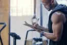 A gym owner reviewing a wall-mounted project timeline with sticky notes during an empty studio build-out, in a natural documentary style.