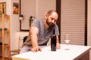 A person labeling wine bottles by hand at a small workbench in a shared production space, shot in a natural documentary style.