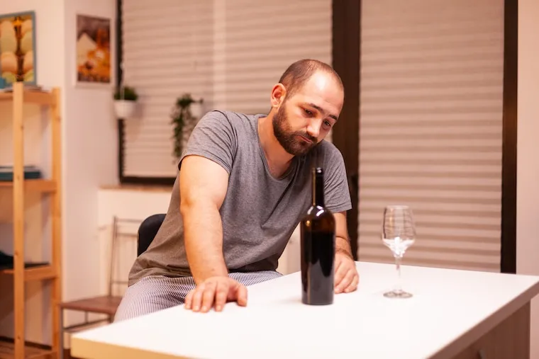 A person labeling wine bottles by hand at a small workbench in a shared production space, shot in a natural documentary style.