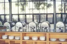 Insulated catering transport carriers, sheet pans, and covered chafing dishes staged on a stainless commissary prep table, in a natural documentary style.