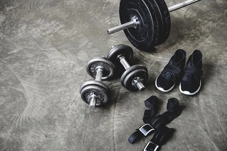 Rows of power racks, barbells, and loaded weight plates on a rubber gym floor, in a natural documentary style.