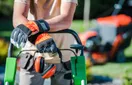 Commercial landscaping equipment lined up on a trailer including a zero-turn mower, string trimmers, and a backpack blower, in a natural documentary style.