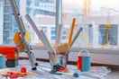 Painting tools laid out on a drop cloth, an airless sprayer, brushes, rollers, and painter's tape, in a natural documentary style.