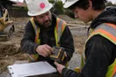 A site contractor showing a new hire a tool technique up close, in a natural documentary style.