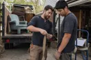 A junk removal operator showing a new hire a tool technique up close, in a natural documentary style.