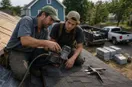 A roofing contractor showing a new hire a tool technique up close, in a natural documentary style.