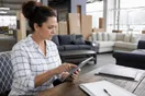 A small business owner in a furniture showroom reviews a delivery company's website on a tablet before signing a contract.