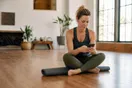 A yoga studio owner sits on a rolled mat in an empty studio checking a slow-loading page on her phone in early morning light, in a natural documentary style.